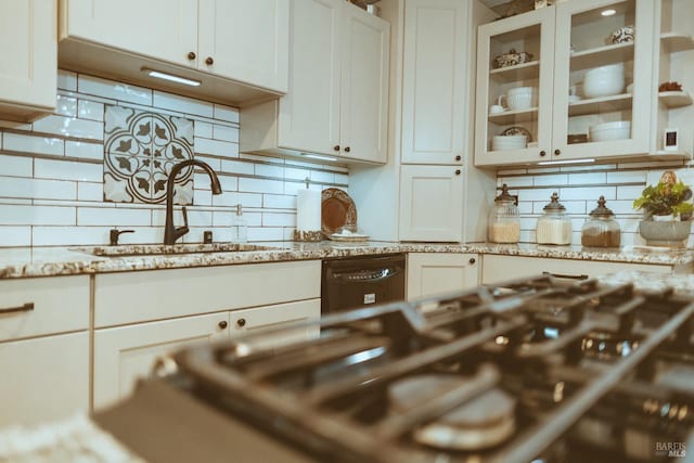 kitchen with a sink, backsplash, glass insert cabinets, white cabinets, and light stone counters