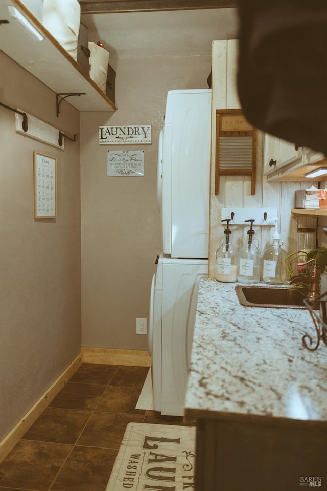 kitchen featuring stacked washer / drying machine, a sink, dark tile patterned floors, and baseboards
