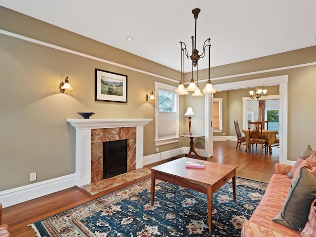 living area featuring an inviting chandelier, baseboards, a high end fireplace, and wood finished floors