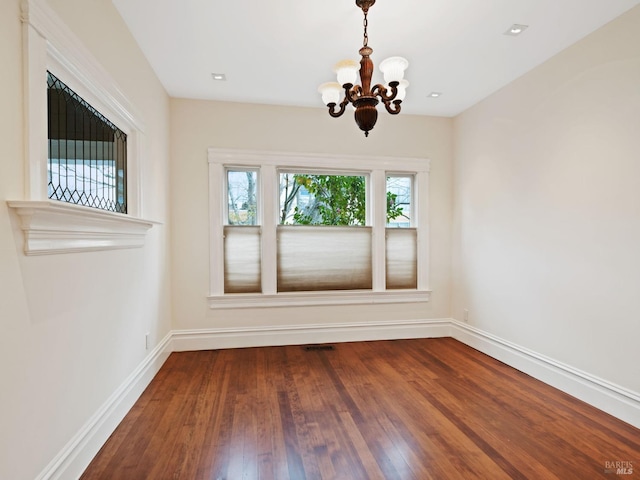 spare room with baseboards, an inviting chandelier, and wood finished floors