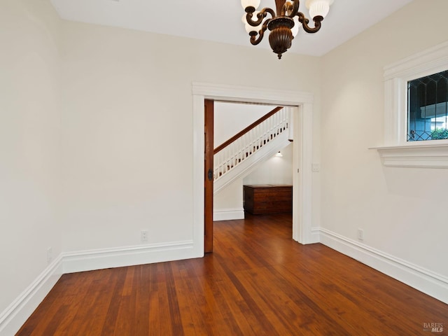 empty room featuring baseboards, an inviting chandelier, wood finished floors, and stairway