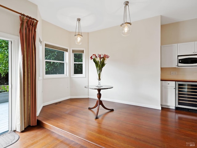 unfurnished dining area featuring beverage cooler, baseboards, and wood finished floors