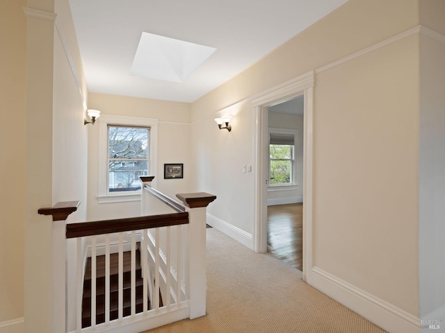 corridor featuring baseboards, carpet flooring, a skylight, and an upstairs landing