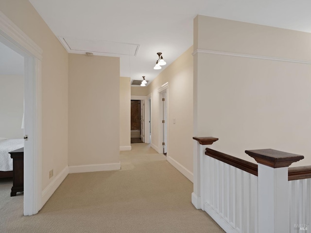 hallway with baseboards, attic access, and light carpet