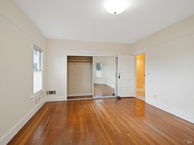 unfurnished bedroom with visible vents, wood-type flooring, baseboards, and a closet