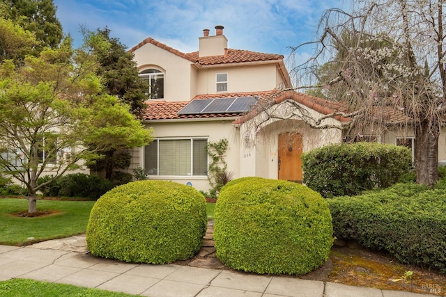 mediterranean / spanish house with a chimney, a tile roof, stucco siding, and solar panels