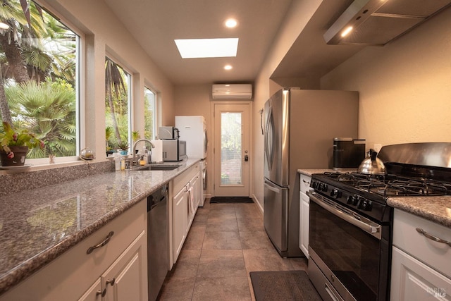 kitchen featuring a sink, a skylight, appliances with stainless steel finishes, under cabinet range hood, and an AC wall unit