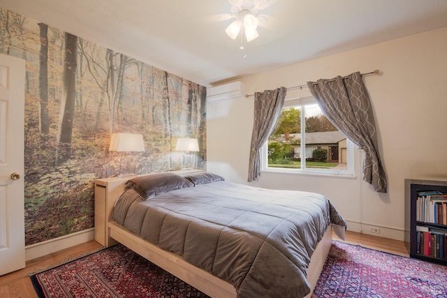 bedroom featuring a wall mounted AC, baseboards, ceiling fan, and wood finished floors
