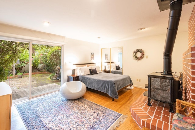 bedroom with baseboards, access to exterior, wood finished floors, and a wood stove