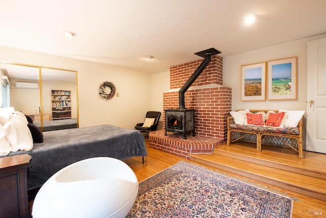 bedroom featuring a closet, a wall mounted AC, wood finished floors, and a wood stove
