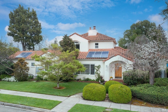 mediterranean / spanish home featuring a tile roof, stucco siding, a front lawn, solar panels, and a chimney