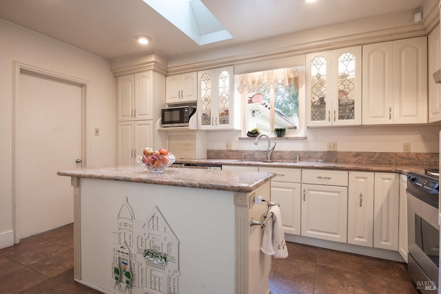 kitchen featuring stainless steel range oven, glass insert cabinets, a skylight, and a sink