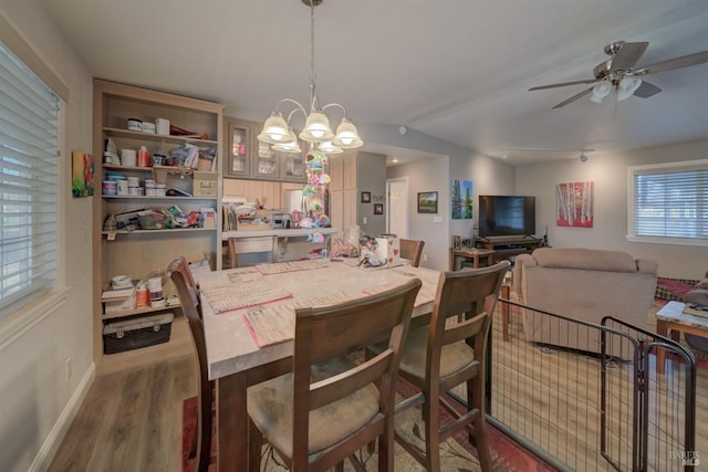 dining space with ceiling fan with notable chandelier, baseboards, and wood finished floors