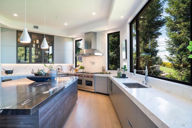 kitchen with double oven range, gray cabinetry, a sink, modern cabinets, and wall chimney exhaust hood