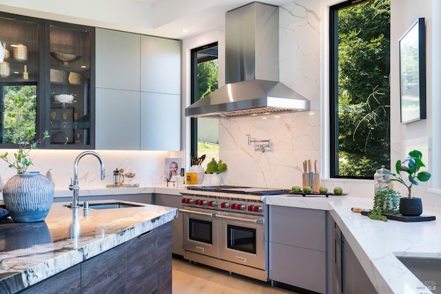 kitchen featuring modern cabinets, a sink, wall chimney exhaust hood, and range with two ovens