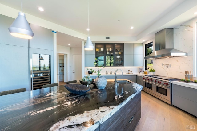 kitchen featuring modern cabinets, a sink, range with two ovens, wall chimney range hood, and gray cabinets