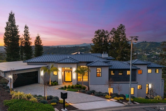 view of front of house with a standing seam roof, stucco siding, an attached garage, metal roof, and decorative driveway