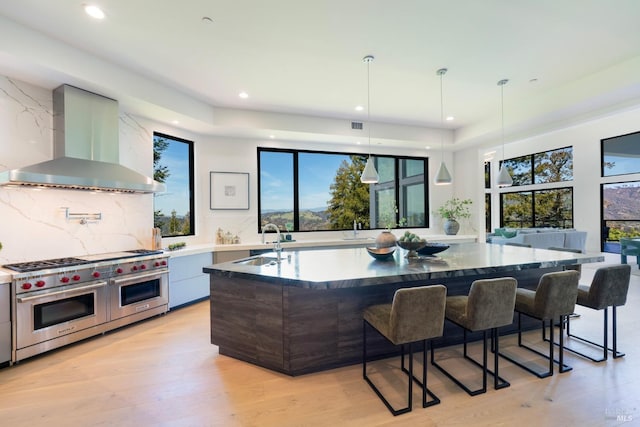 kitchen with double oven range, a sink, a large island, wall chimney range hood, and modern cabinets