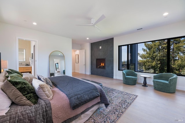 bedroom featuring recessed lighting, baseboards, connected bathroom, a fireplace, and wood finished floors