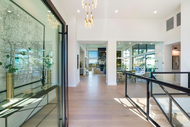 hall featuring a notable chandelier, a high ceiling, wood finished floors, baseboards, and recessed lighting