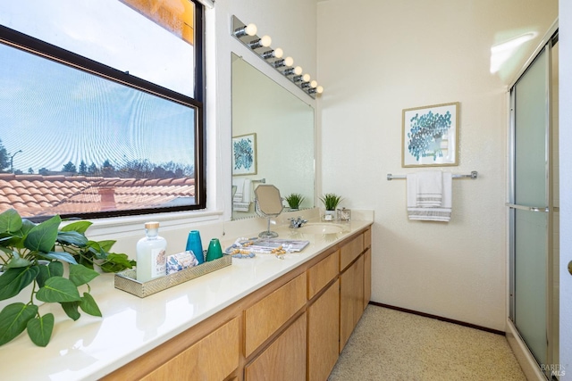 bathroom with baseboards, a shower with shower door, a sink, and double vanity