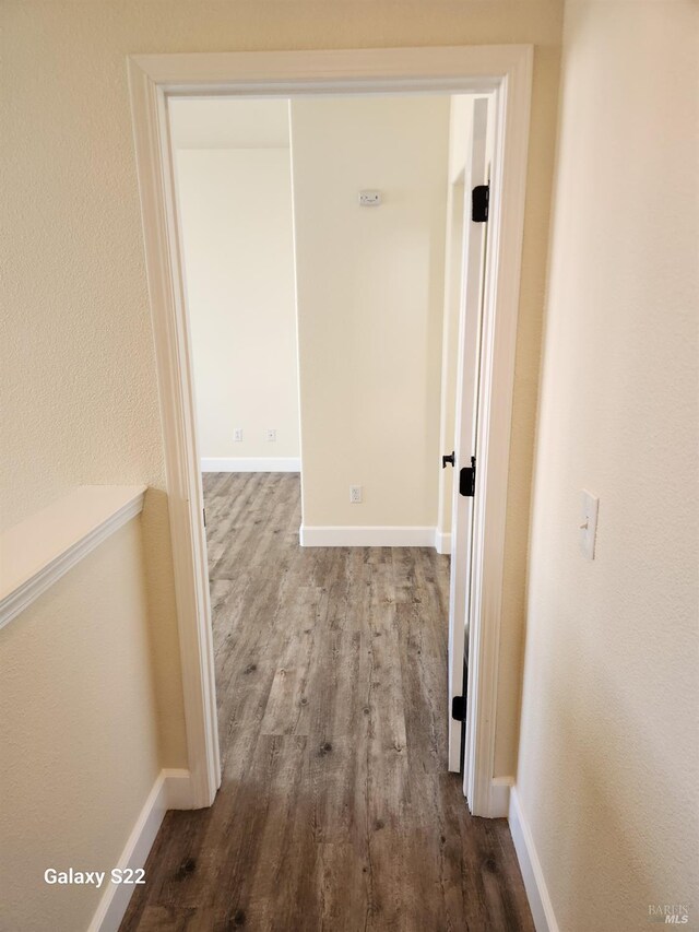 kitchen with stainless steel dishwasher, a sink, dark wood-type flooring, baseboards, and a center island with sink