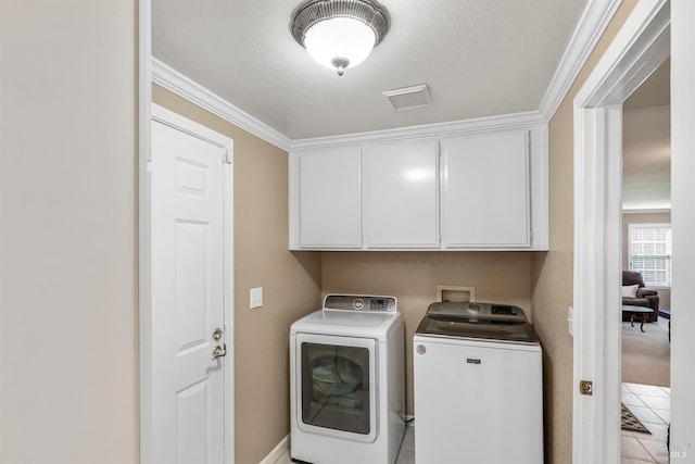 washroom with washing machine and dryer, a textured ceiling, cabinet space, and ornamental molding
