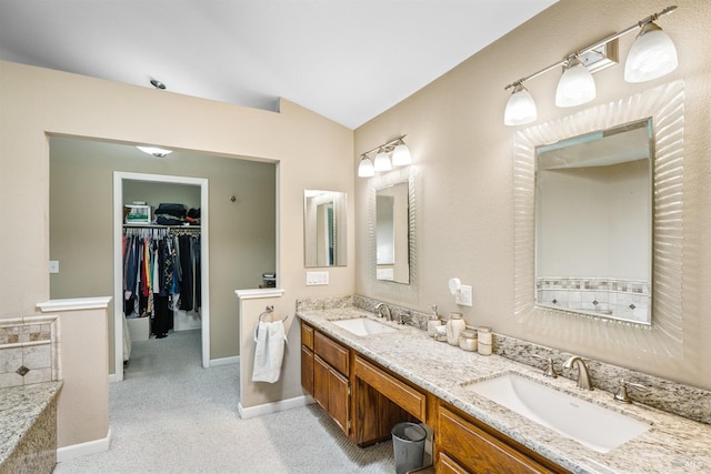 bathroom with double vanity, vaulted ceiling, a spacious closet, and a sink