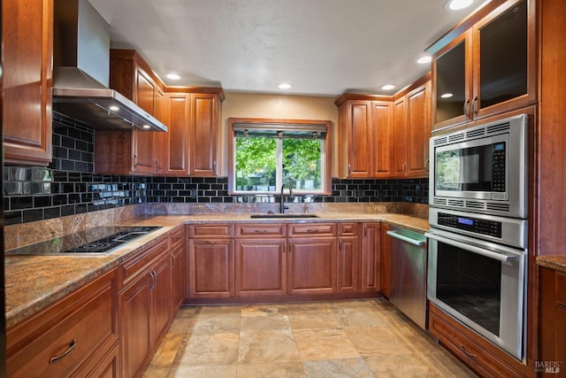 kitchen with wall chimney range hood, tasteful backsplash, a sink, brown cabinets, and stainless steel appliances