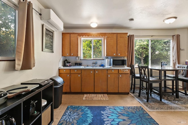 kitchen with brown cabinets, light countertops, stainless steel microwave, and a wall mounted air conditioner