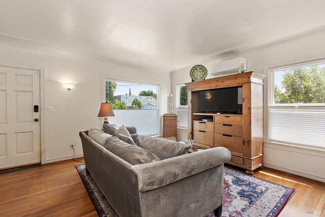 living room with an AC wall unit, baseboards, plenty of natural light, and wood finished floors