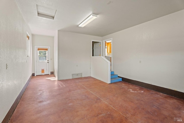 spare room with finished concrete flooring, attic access, baseboards, and stairway