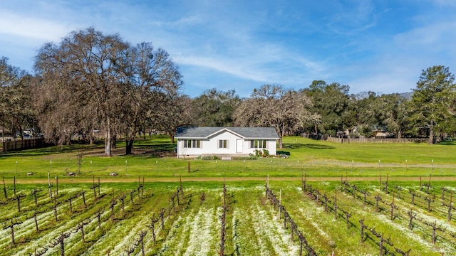 rear view of house with fence, a lawn, and a rural view