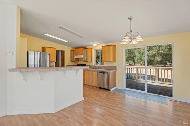 kitchen with a kitchen breakfast bar, a peninsula, light wood-style flooring, stainless steel appliances, and tile countertops
