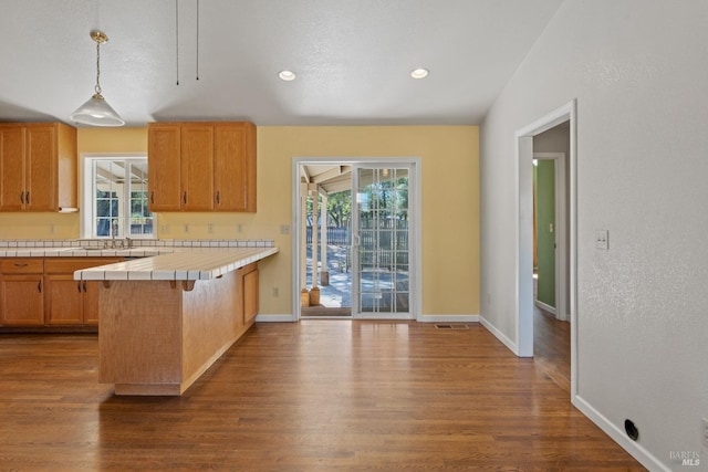kitchen featuring pendant lighting, dark wood finished floors, a kitchen breakfast bar, tile counters, and baseboards