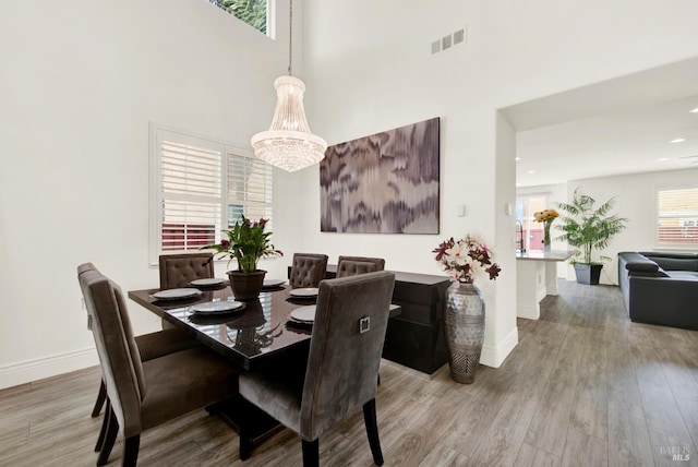 dining area featuring baseboards, a high ceiling, visible vents, and wood finished floors