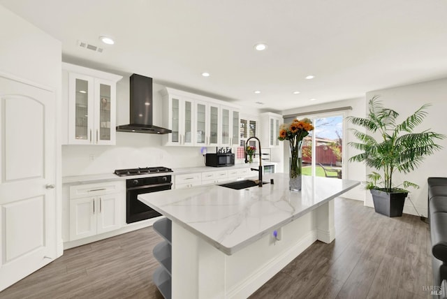 kitchen with wall oven, wall chimney exhaust hood, a center island with sink, a sink, and black microwave