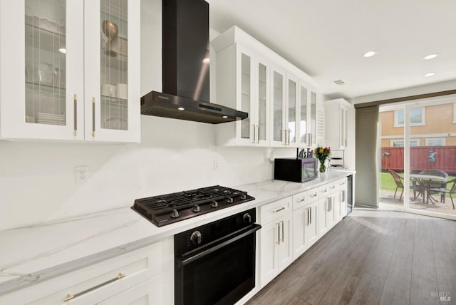 kitchen featuring white cabinetry, light stone countertops, black appliances, and wall chimney exhaust hood