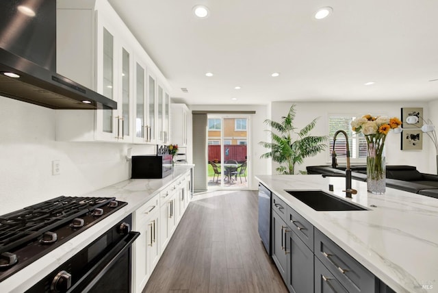 kitchen featuring range, dishwasher, wall chimney exhaust hood, white cabinetry, and a sink