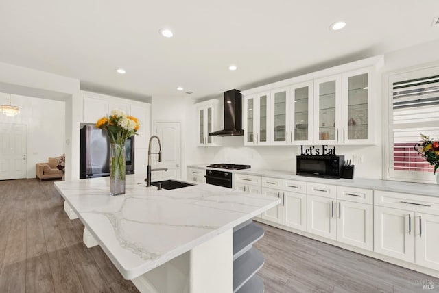 kitchen with a sink, light wood-style floors, freestanding refrigerator, black microwave, and wall chimney exhaust hood