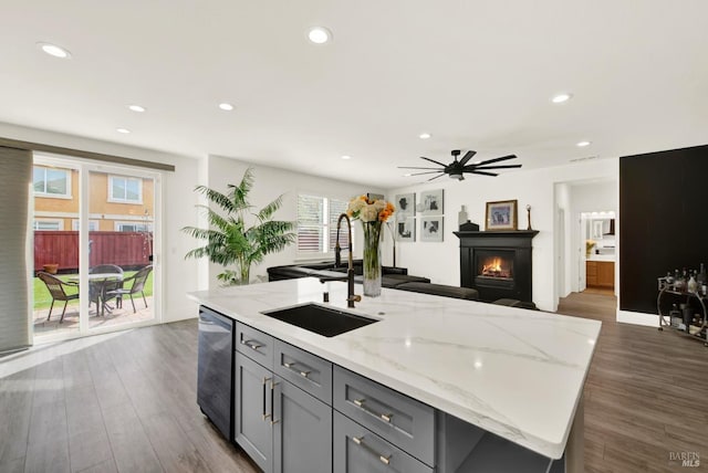 kitchen with gray cabinets, a sink, a warm lit fireplace, stainless steel dishwasher, and recessed lighting