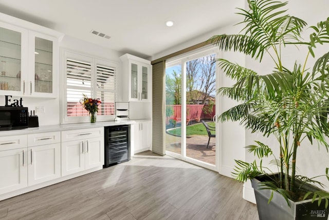 bar featuring wet bar, wine cooler, black microwave, light wood-style flooring, and visible vents