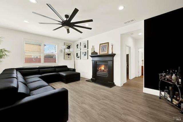 living area with wood finished floors, a glass covered fireplace, visible vents, ceiling fan, and recessed lighting