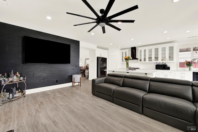 living room with ceiling fan, an accent wall, recessed lighting, and light wood finished floors
