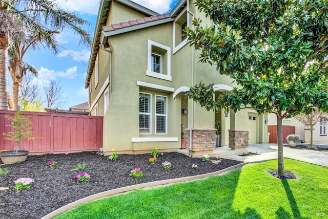 view of front of home featuring stucco siding, stone siding, fence, and concrete driveway