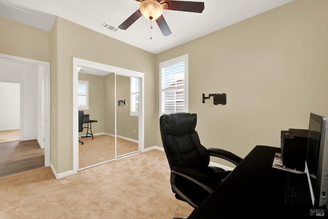 carpeted office space featuring baseboards, visible vents, and ceiling fan