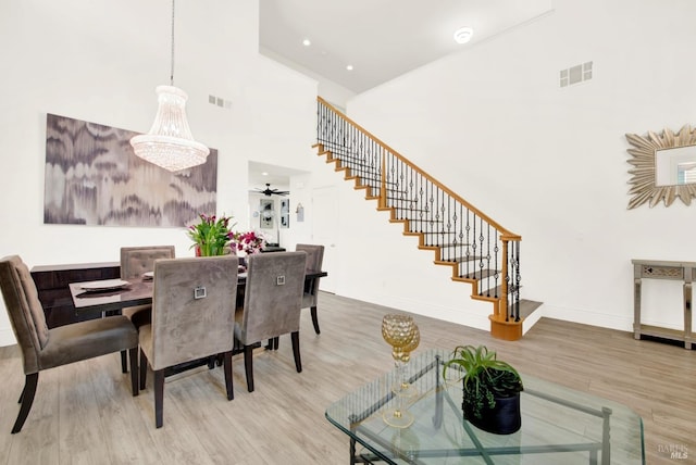 dining area with stairway, a high ceiling, wood finished floors, baseboards, and visible vents