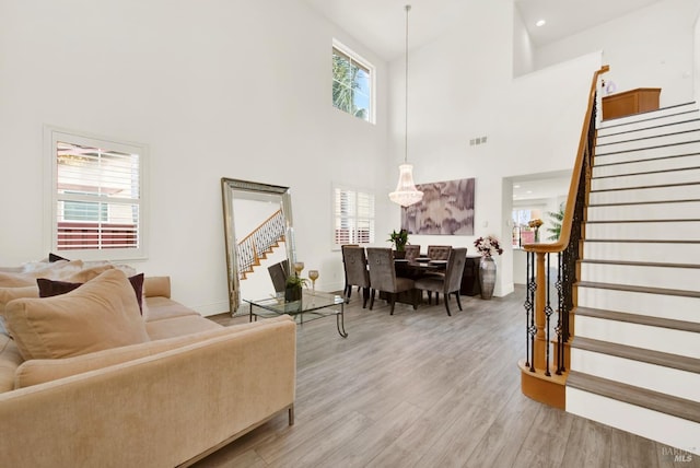 living room with light wood finished floors, visible vents, a towering ceiling, and stairway