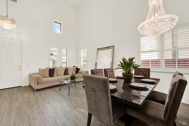 dining space with an inviting chandelier, a towering ceiling, and wood finished floors