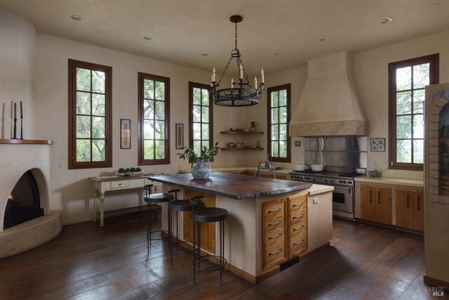 kitchen with a warm lit fireplace, dark wood-type flooring, a center island, custom range hood, and stainless steel stove